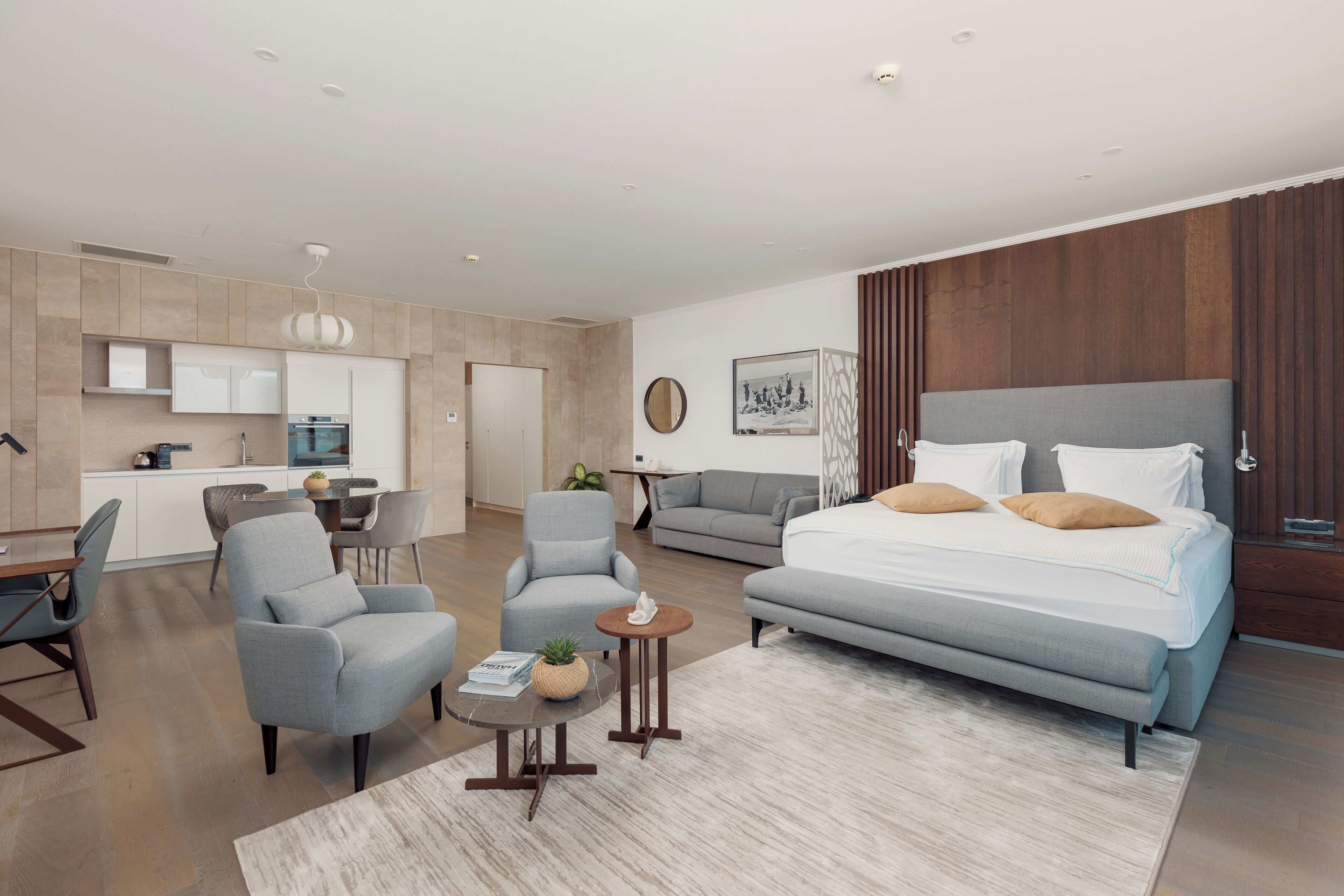 A modern hotel room with a large bed, a sofa, a dining area, and a kitchen.