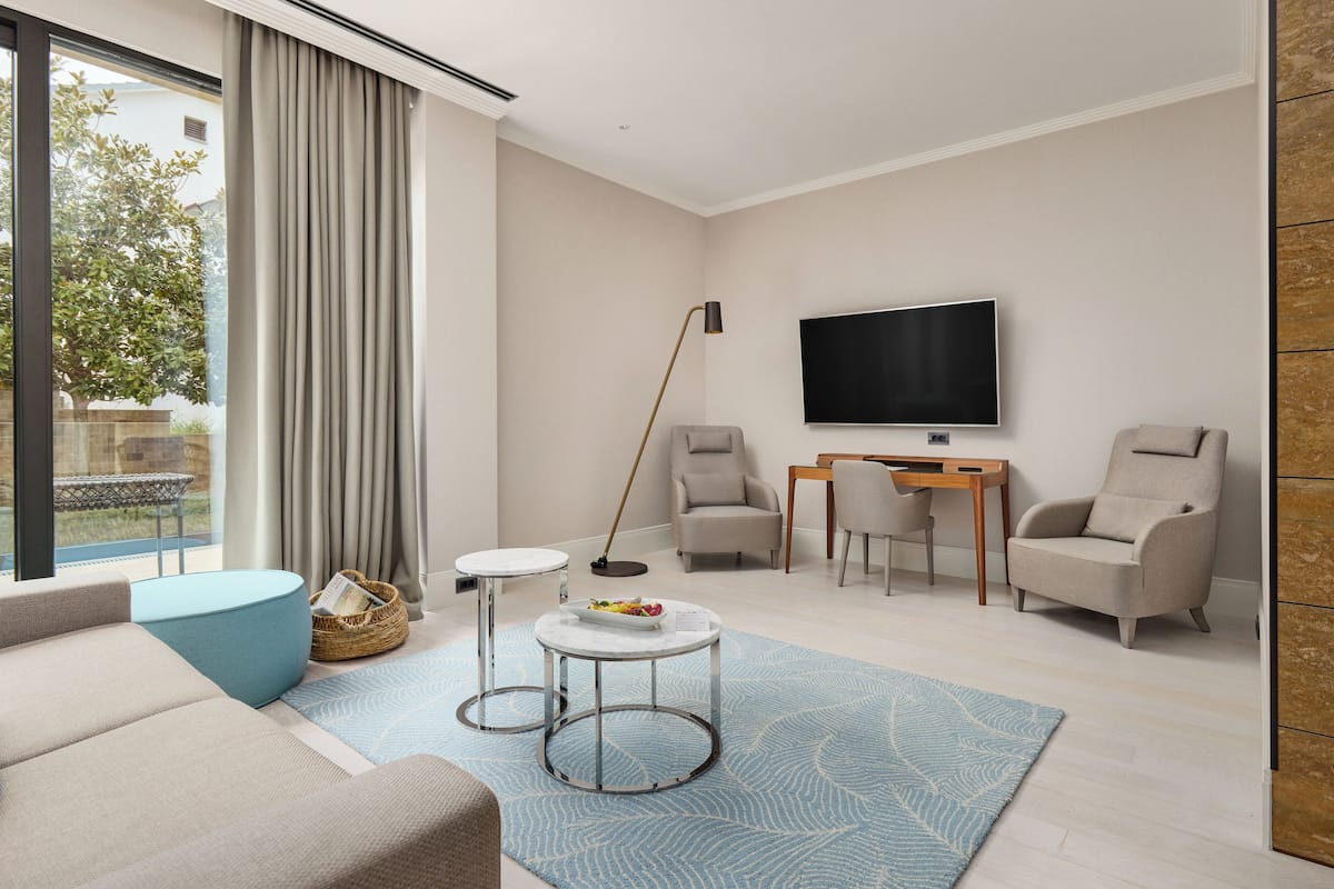 A modern living room with a sofa, two armchairs, a coffee table, a TV, and a floor lamp.