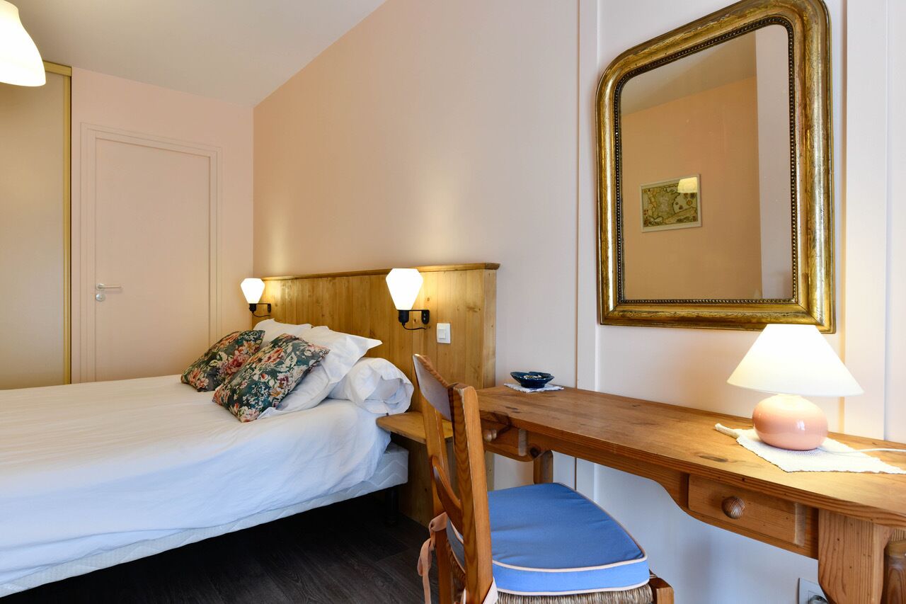 Un dormitorio con cama, un escritorio de madera, una silla, una lámpara y un espejo.