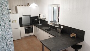 Cocina compacta con armarios blancos, horno Bosch, microondas, lavabo y tostadora.