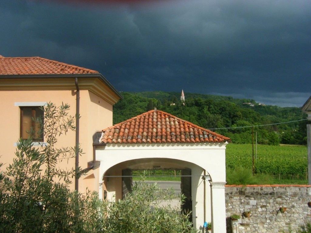 A building with a tiled roof and an archway, surrounded by greenery and a stone wall.