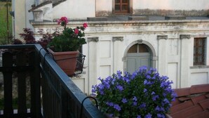 Un bâtiment à la façade blanche, doté d’une petite fenêtre avec une porte en bois et d’un balcon orné de plantes en pot.