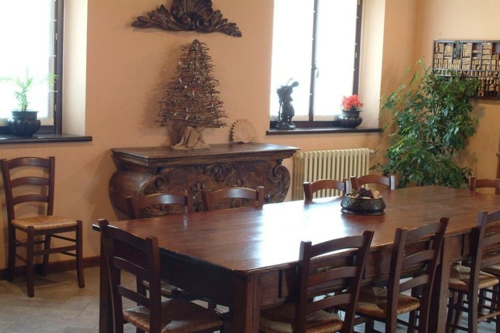 Une salle à manger avec une grande table en bois, six chaises, un arbre décoratif et une bibliothèque.