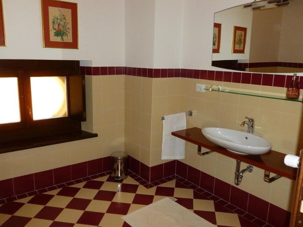Un baño con piso a cuadros, un lavamanos con espejo arriba y una ventana con cortina.