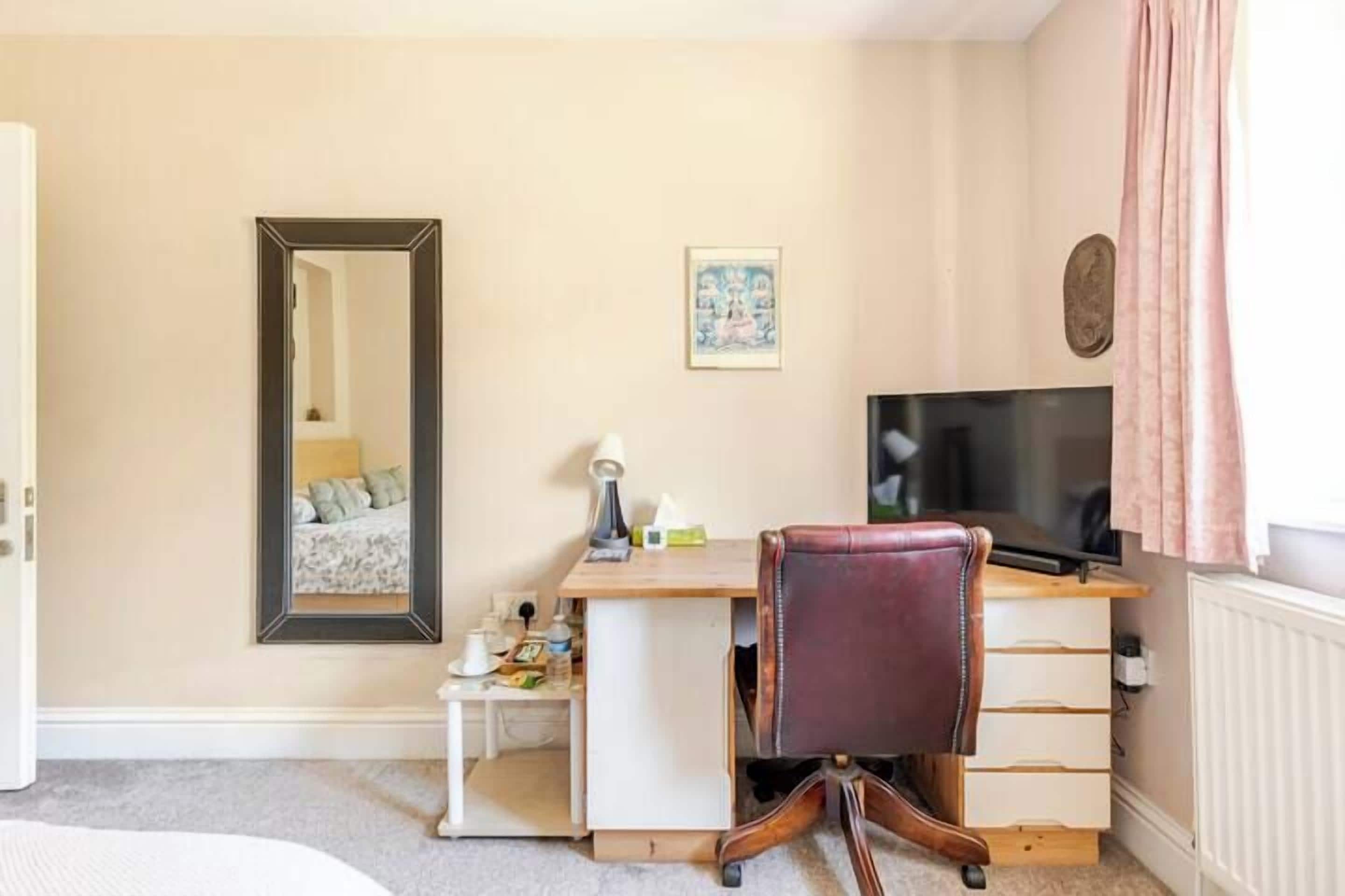 Un dormitorio con cama, escritorio, silla, televisor y espejo.