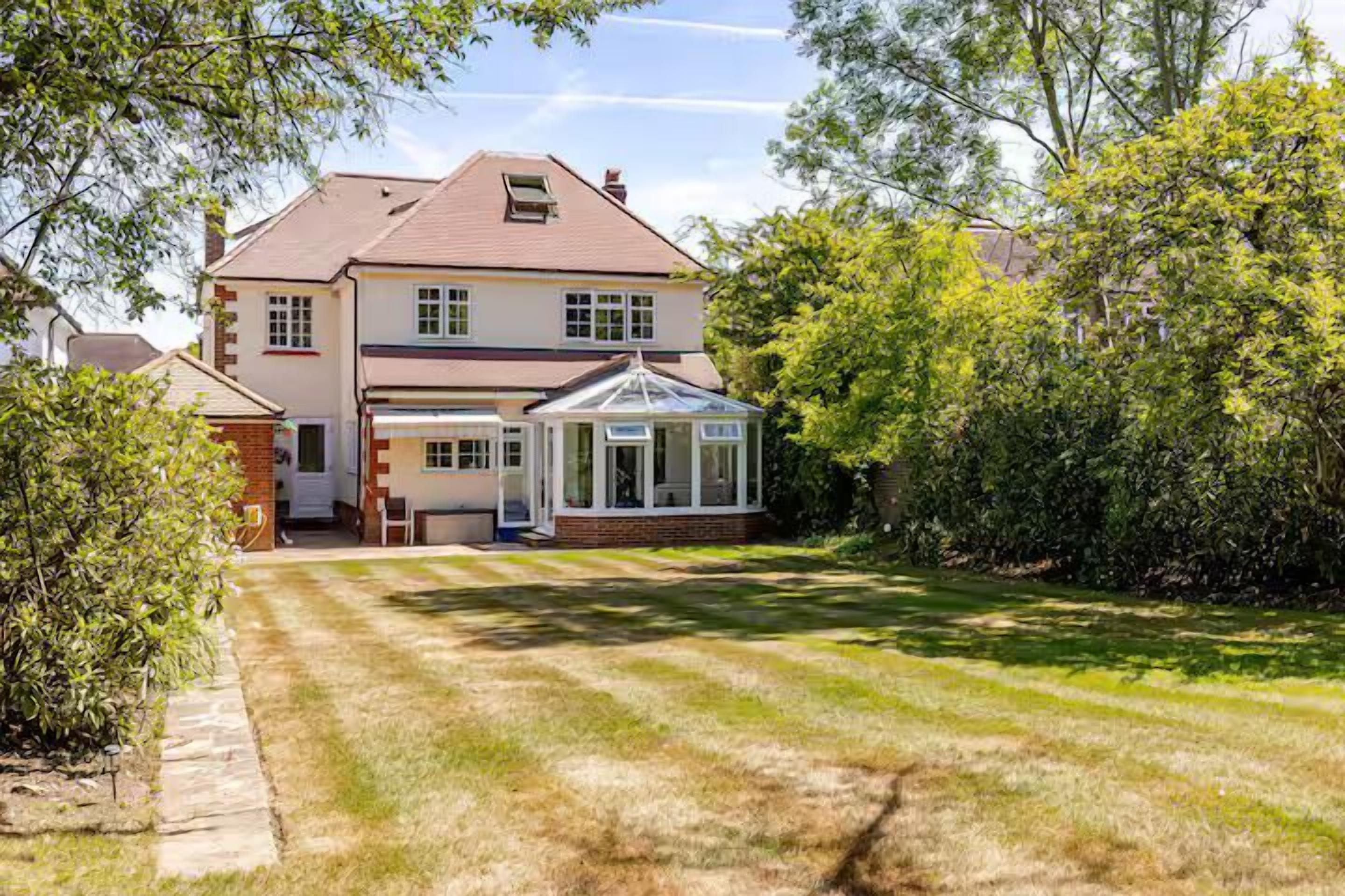 Une maison à deux étages dotée d’une véranda, d’une pelouse bien entretenue et d’arbres adultes.