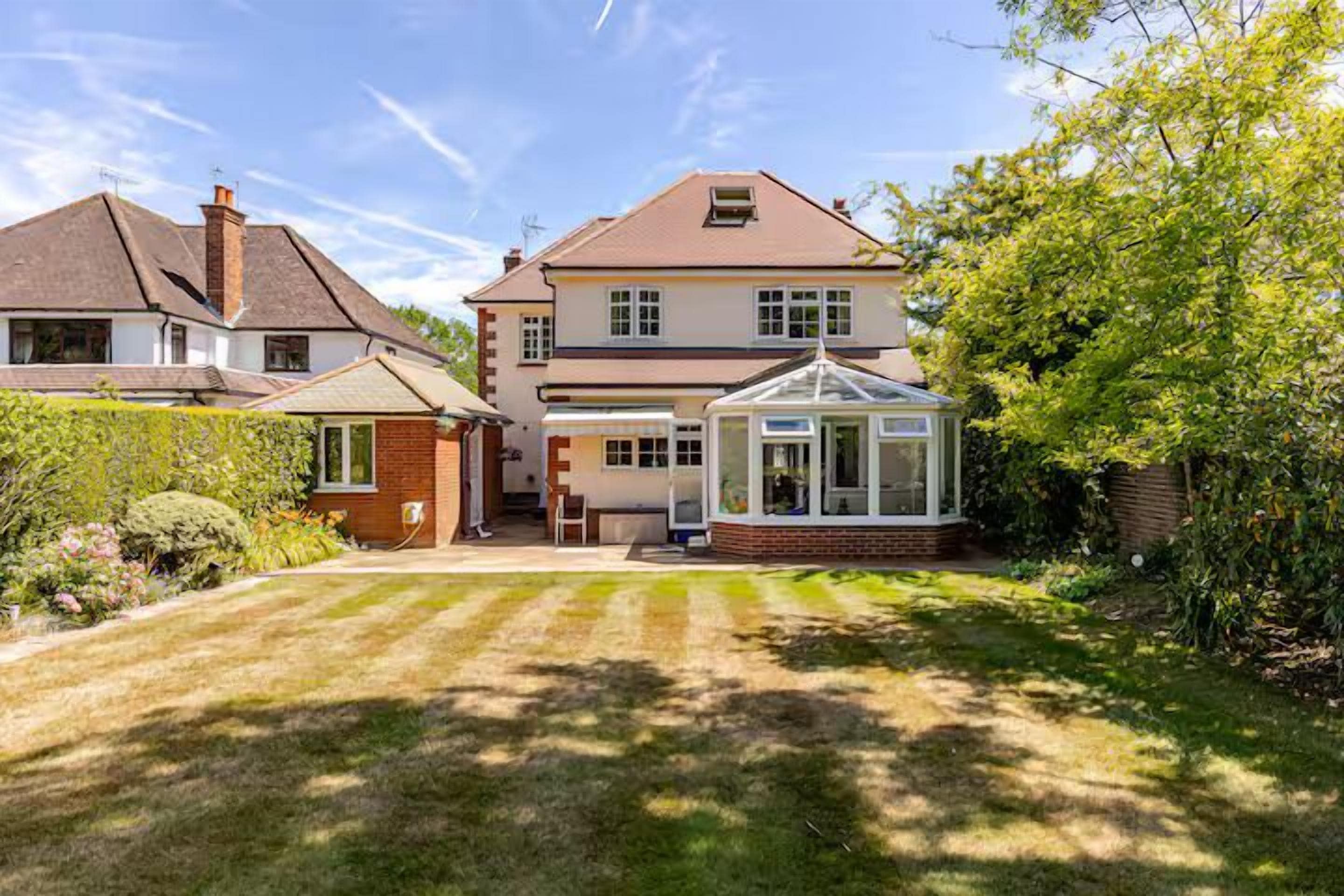 A two-story house with a conservatory, a well-maintained lawn, and a brick wall.