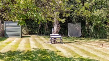 Un jardin avec un arbre, une table abritée et un abri de jardin.