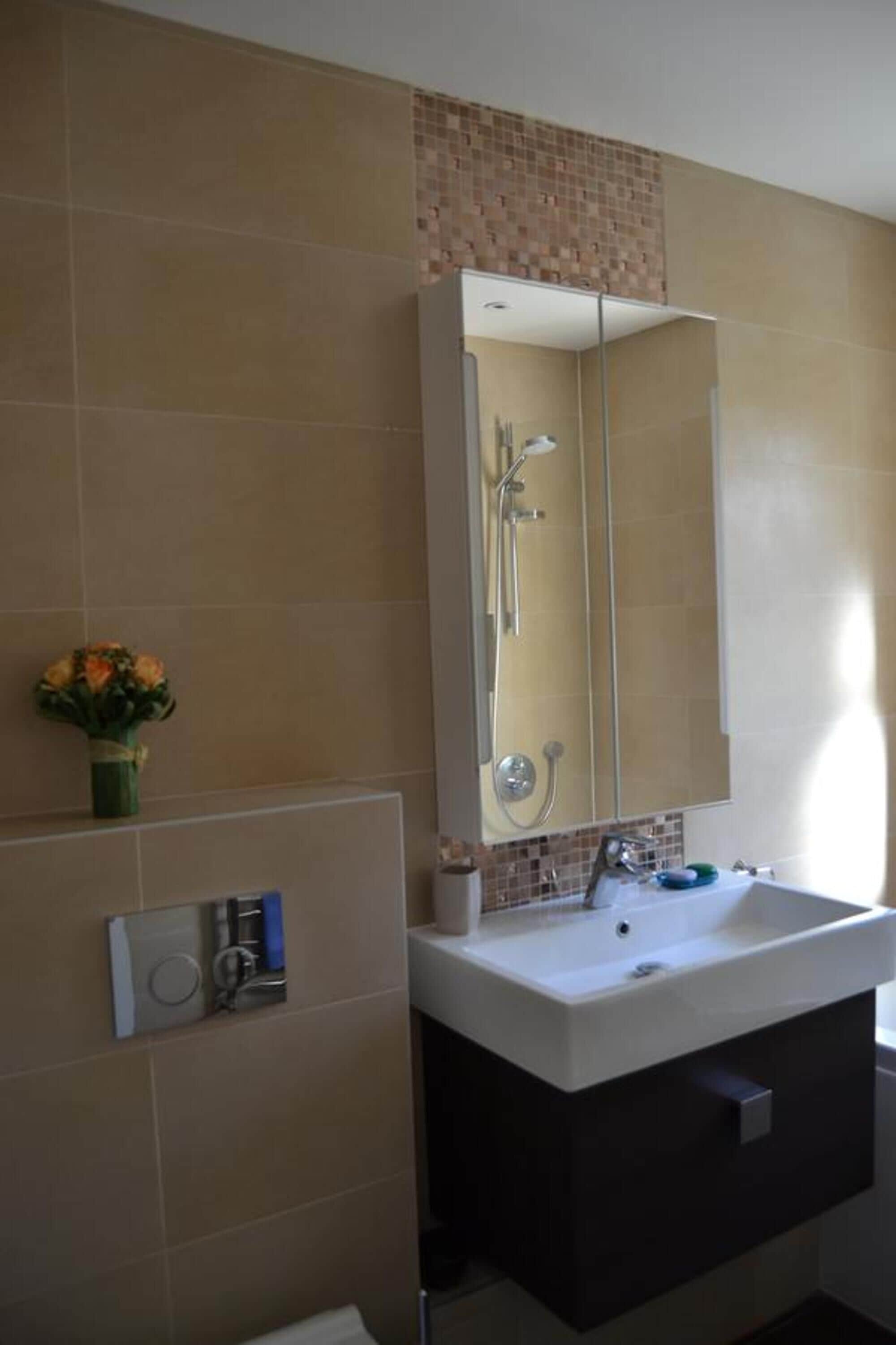 A bathroom with a large mirror, a sink, and a shower.