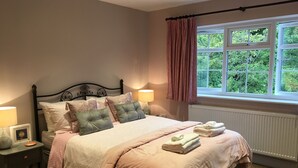 Une chambre à coucher avec un lit, des tables de chevet, une fenêtre avec des rideaux et une vue sur la verdure à l’extérieur.