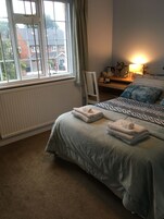 Un dormitorio con cama, una silla, una mesita de noche, una lámpara y vistas al exterior.