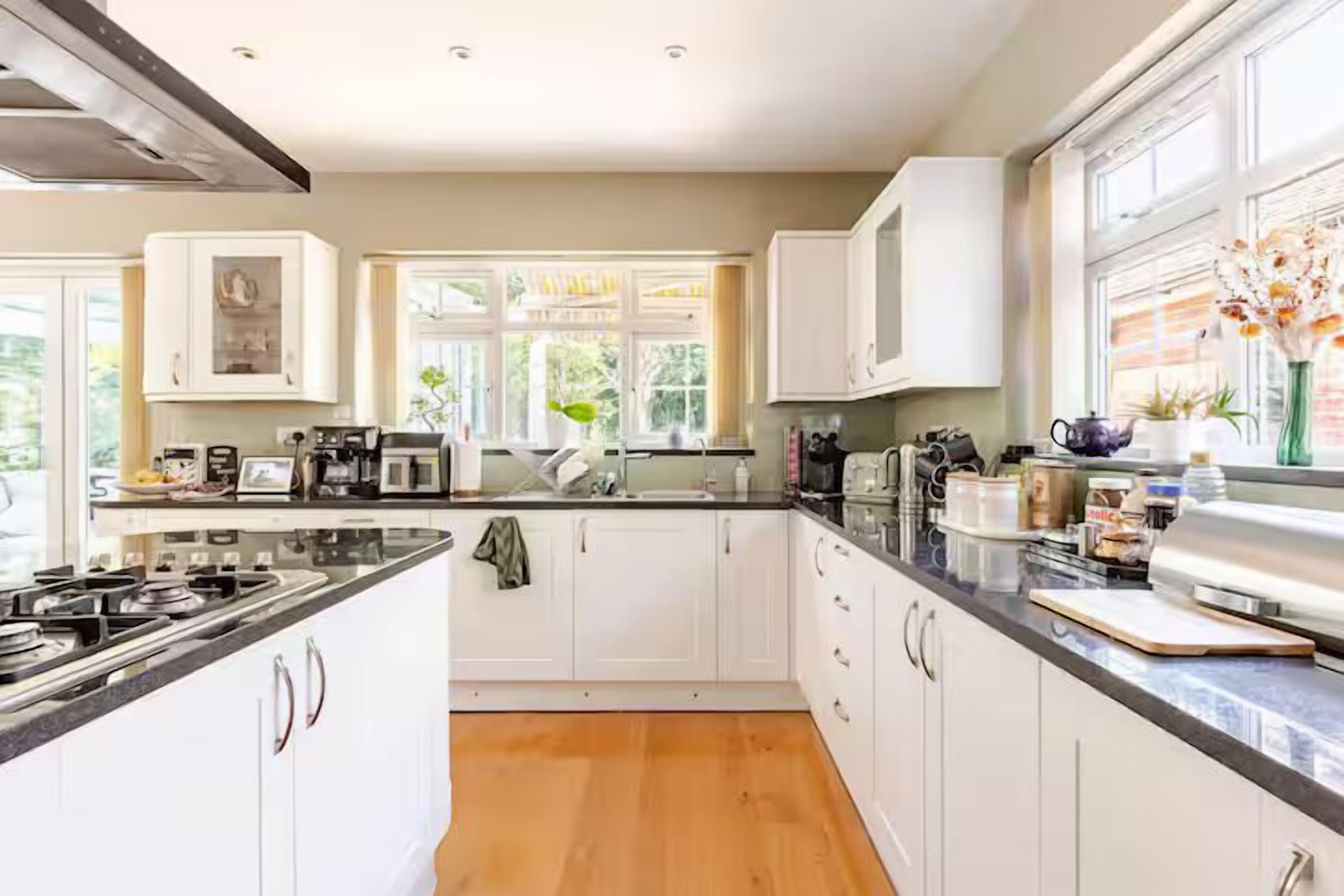 A modern kitchen with white cabinetry, a black countertop, and a wooden floor.
