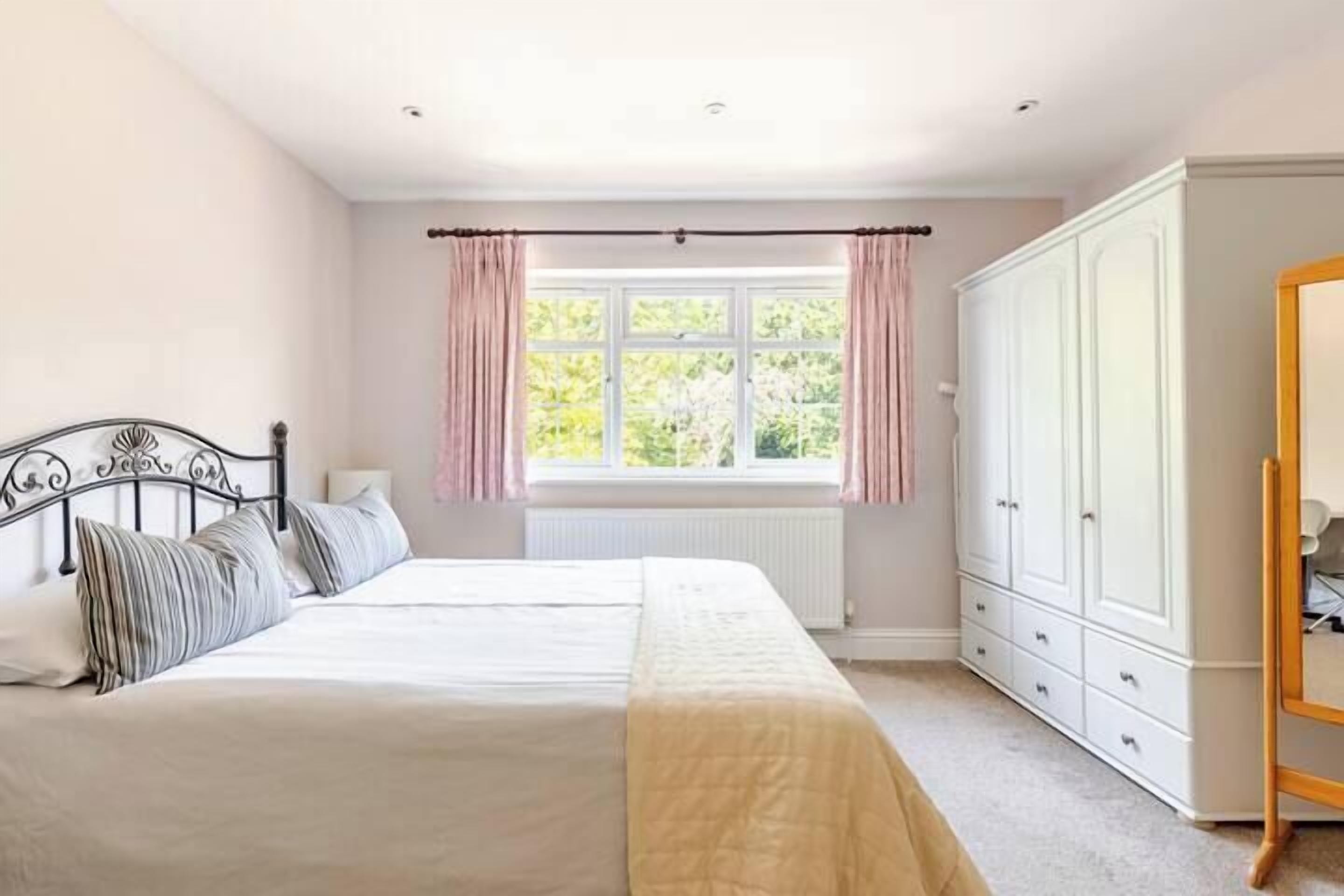 Un dormitorio con cama doble, armario y ventana con cortinas.