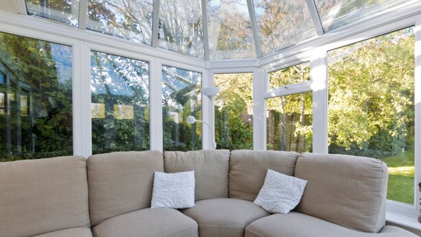 Un canapé d’angle avec des coussins, un plafond en verre et une vue sur un jardin.
