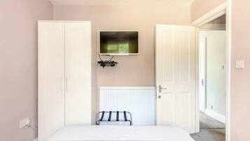 A bedroom with a bed, a radiator, a television mounted on the wall, and a wardrobe.