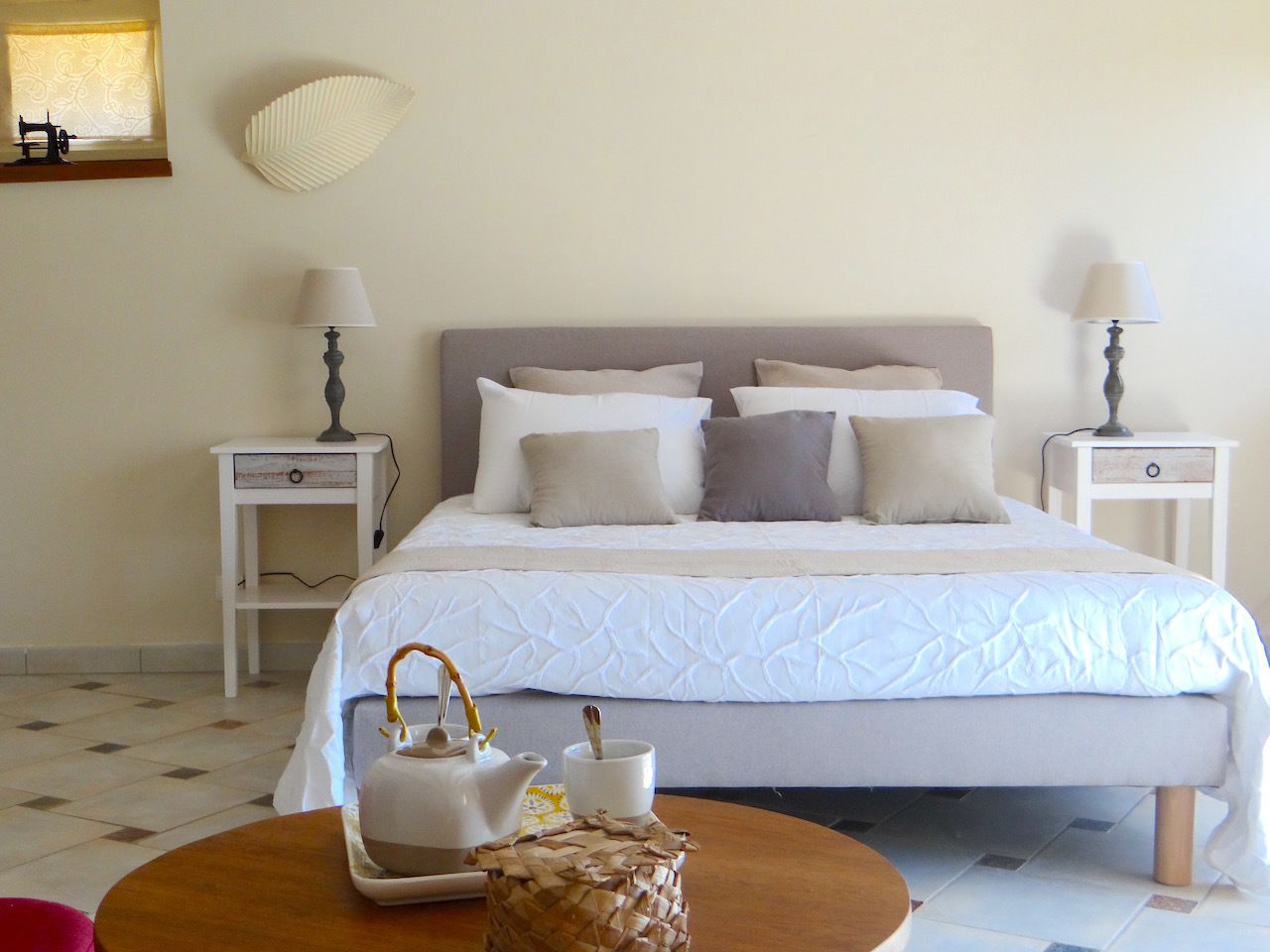 A neatly arranged bedroom with a bed, bedside tables, a lamp, and a small table with a teapot and cup.