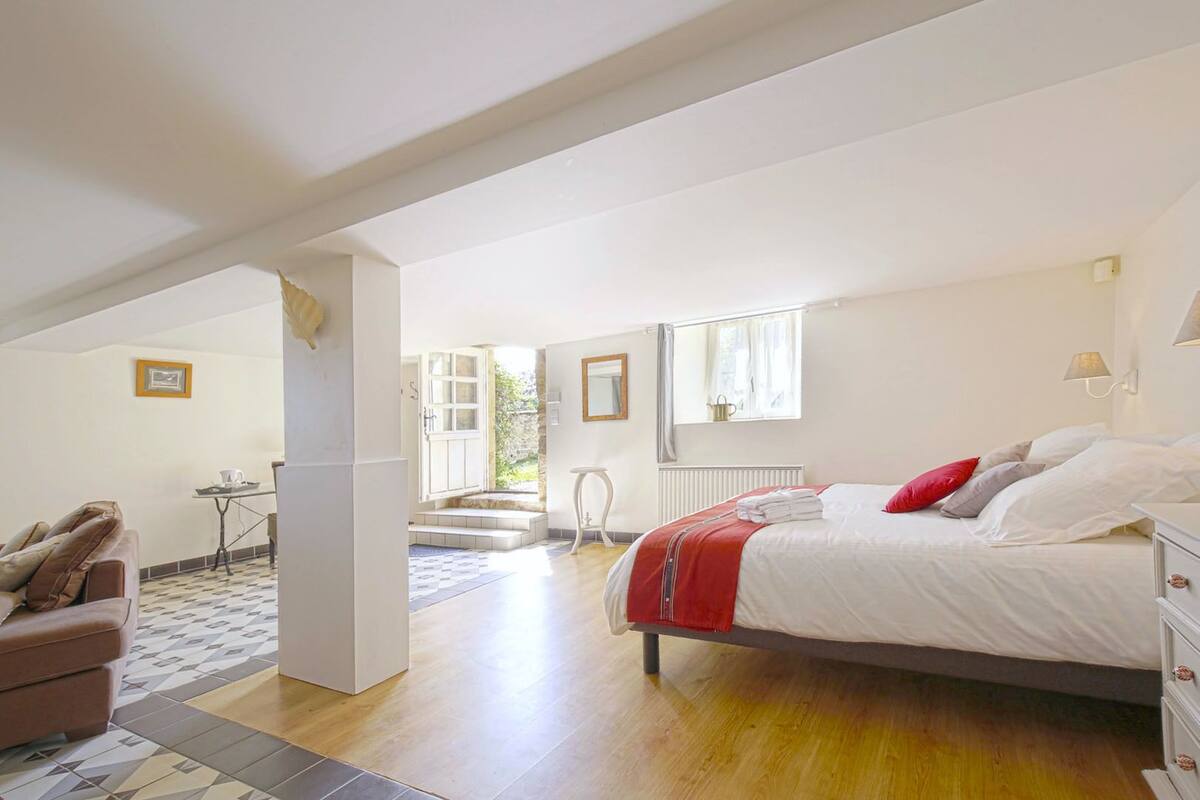 Une chambre spacieuse avec un grand lit, un coin salon avec un canapé et une vue sur l’extérieur grâce à une porte ouverte.