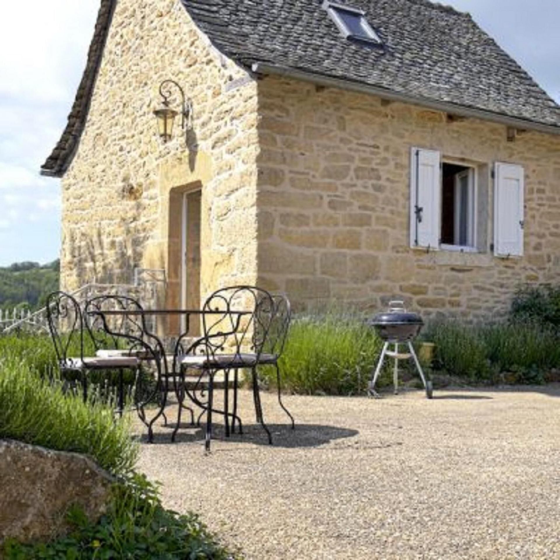 A stone house with a gravel patio, a table with chairs, and a barbecue grill.