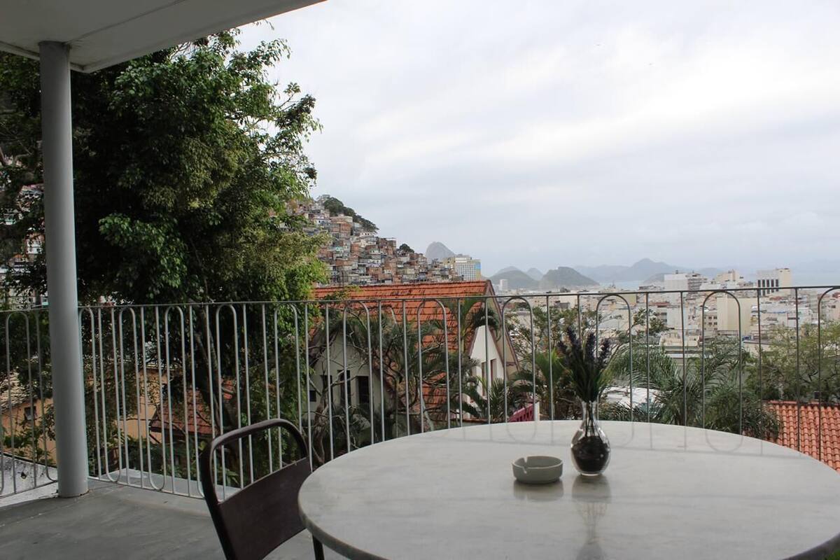 Un balcón con una mesa redonda y sillas, con vista a una ciudad densamente poblada, con edificios y montañas a lo lejos.