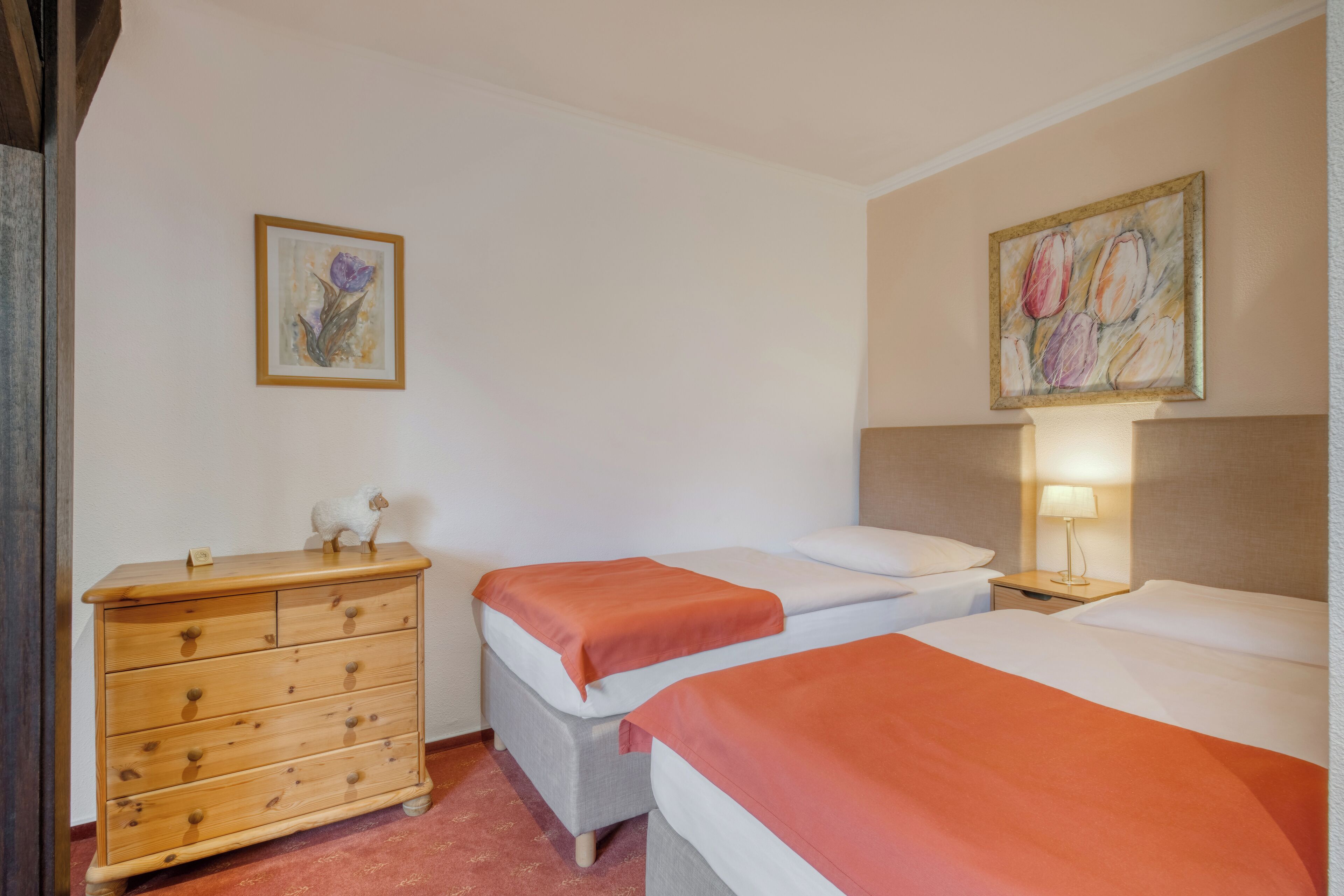 Een hotelkamer met twee bedden, een houten dressoir en een nachtkastje met een lamp.