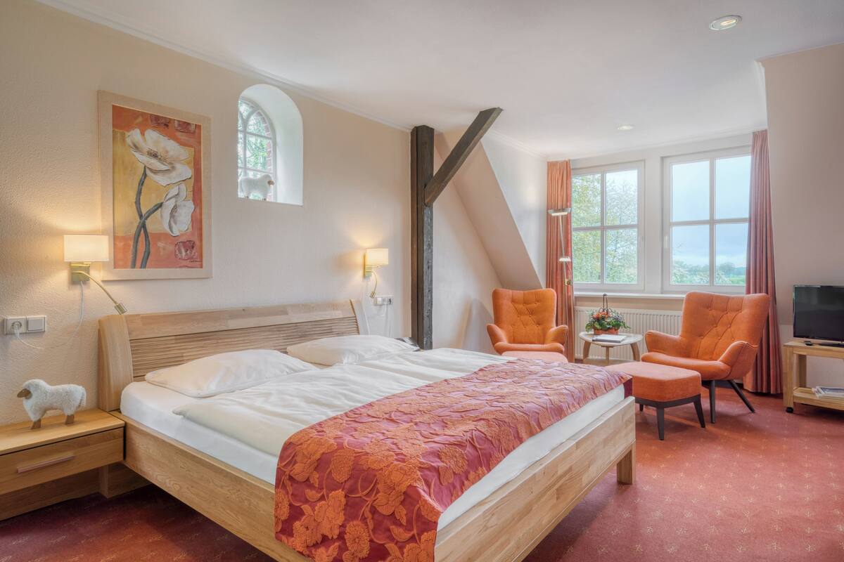 Una habitación de hotel con una cama grande, dos sillas, un televisor y un cuadro en la pared.