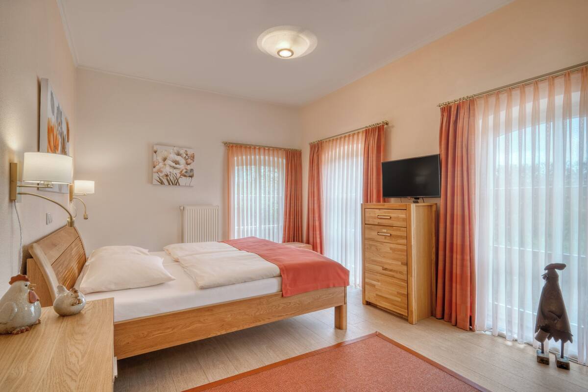 Un dormitorio con cama de madera, cómoda, televisor y ventana con cortinas.