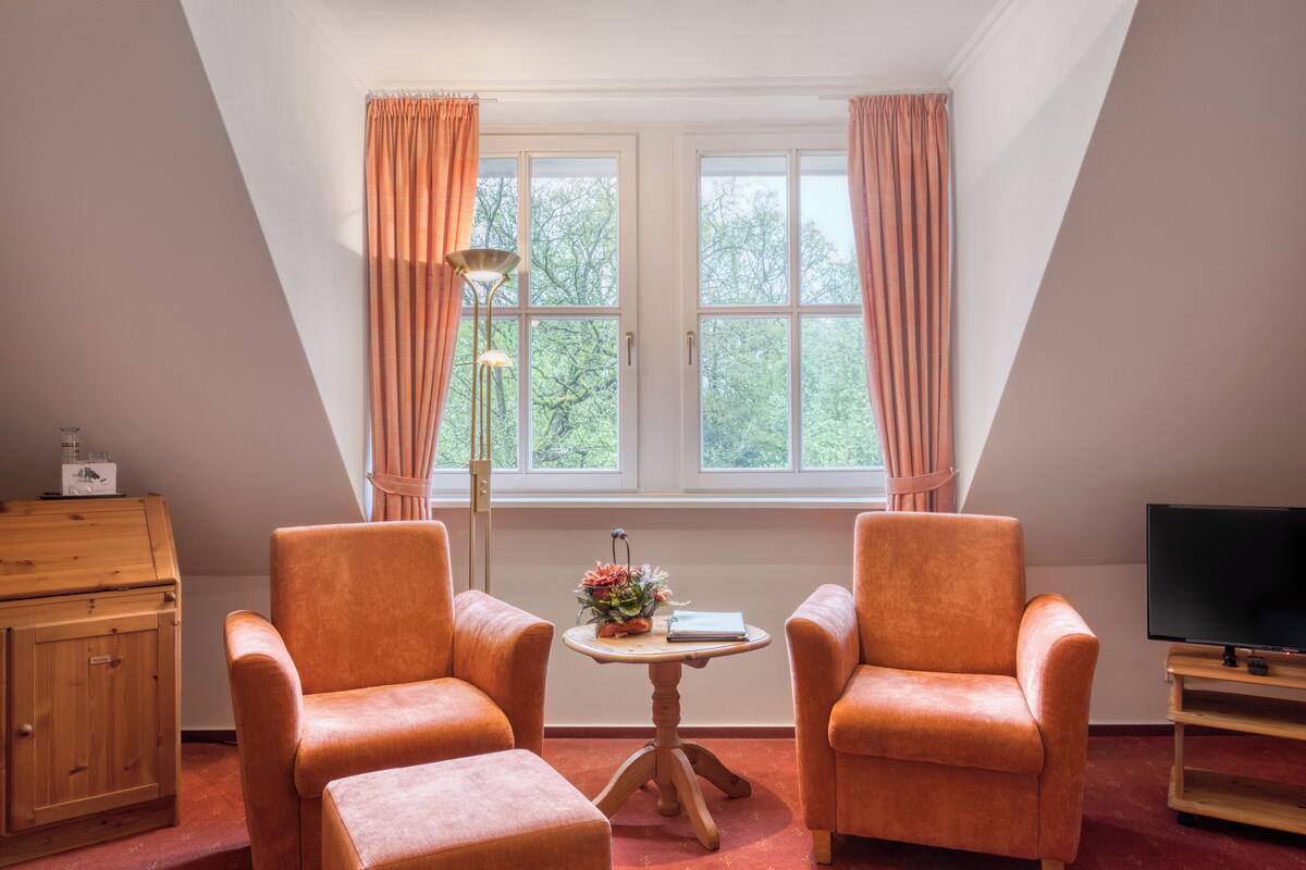 Una habitación acogedora con dos sillones naranjas, una mesita con un jarrón, un armario de madera y un mueble para televisión.