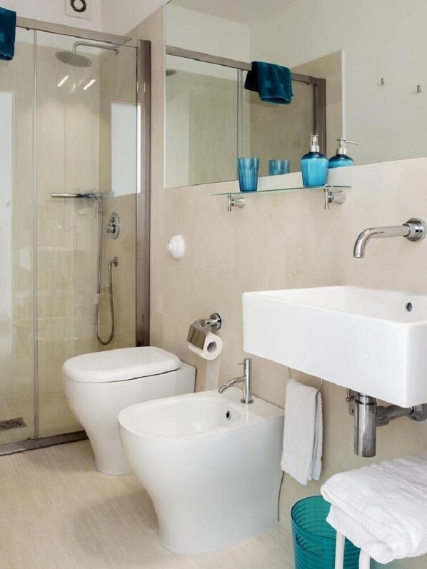 A modern bathroom with a glass shower enclosure, a toilet, a bidet, and a sink with a mirror above. - B&B Do'mmilio (Crotone)