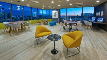 Um espaço de escritório moderno com grandes janelas, diversas opções de assento e vista para a cidade.