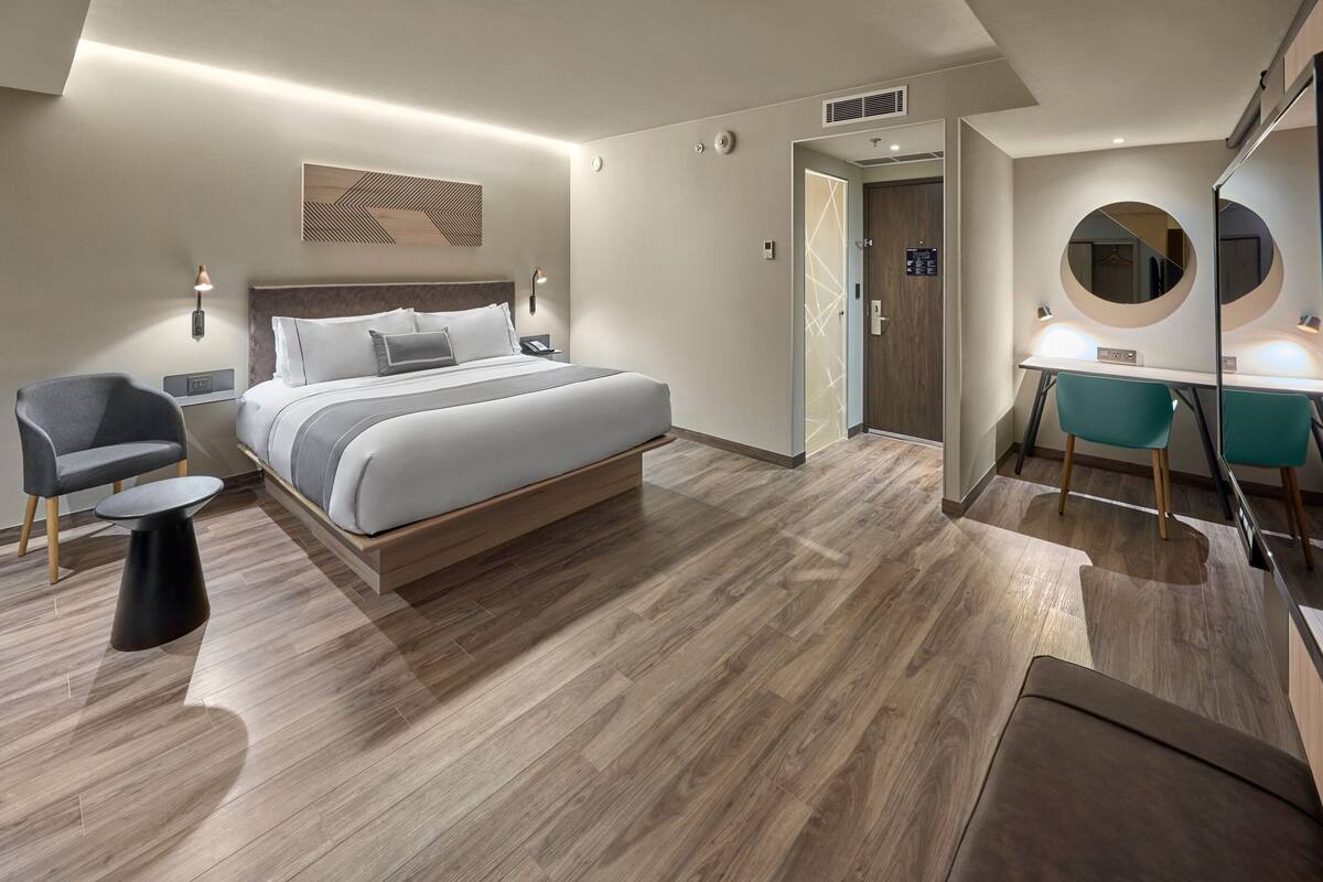 Una habitación de hotel moderna con una cama grande, un escritorio con espejo, una silla y una pequeña mesa.