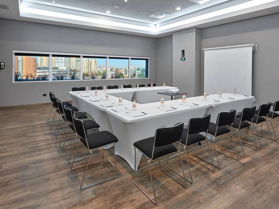 Un salón de conferencias con una larga mesa, sillas negras y una pantalla para proyector.