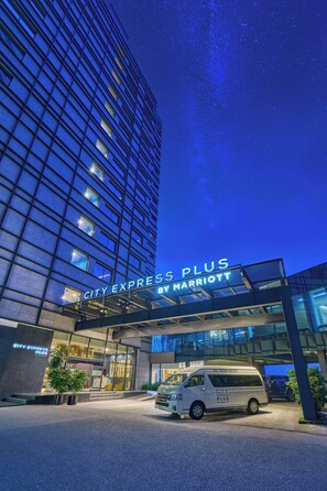 L’entrée d’un hôtel, avec une façade moderne en verre et une enseigne indiquant « City Express Plus by Marriott ».