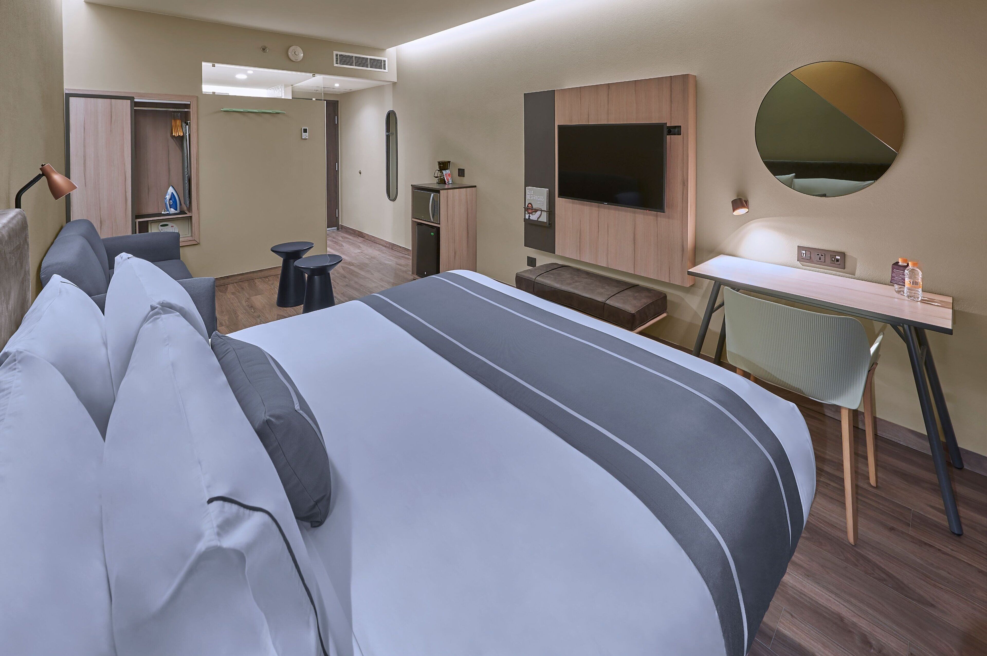 Quarto de hotel moderno com uma cama grande, uma escrivaninha, uma cadeira, uma televisão e um guarda-roupa.