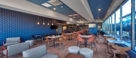 A modern restaurant with a blue patterned wall, wooden tables, and comfortable seating.
