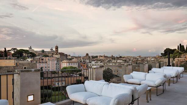 A rooftop terrace with white cushioned seating and a view of a cityscape. - Rhinoceros (Rome)
