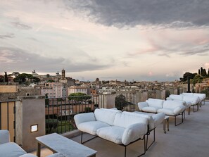 Terraza en la azotea con asientos blancos acolchados y vistas a un paisaje urbano.