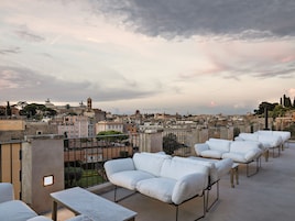A rooftop terrace with white cushioned seating and a view of a cityscape.