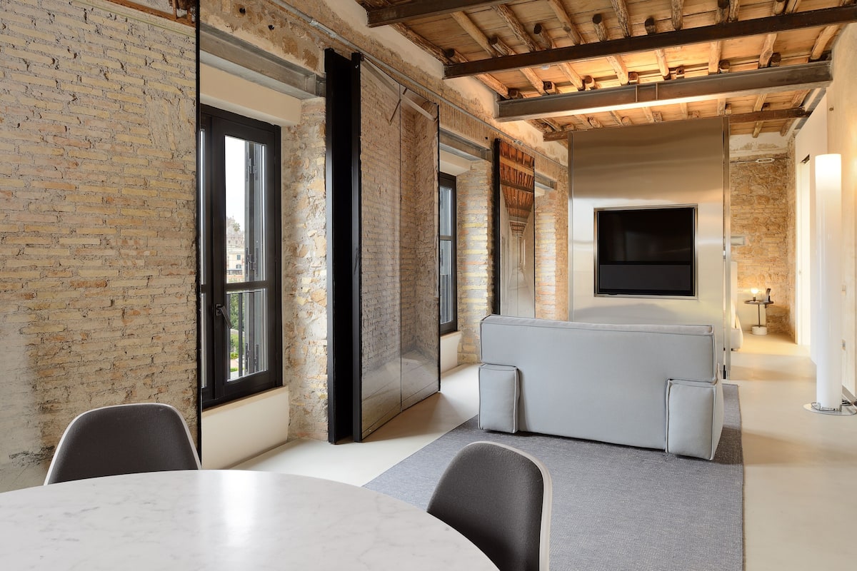 A modern room with a brick wall, a large window, a flat-screen TV, and a seating area.