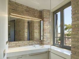 A bathroom with a white sink, a large mirror, and a brick wall.
