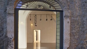 An arched doorway leading into a building with a stone wall and a metal staircase. - Rhinoceros (Rome)