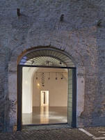 An arched doorway leading into a building with a stone wall and a metal staircase.