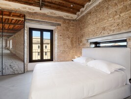 A bedroom with a large bed, a brick wall, and a window overlooking a building.