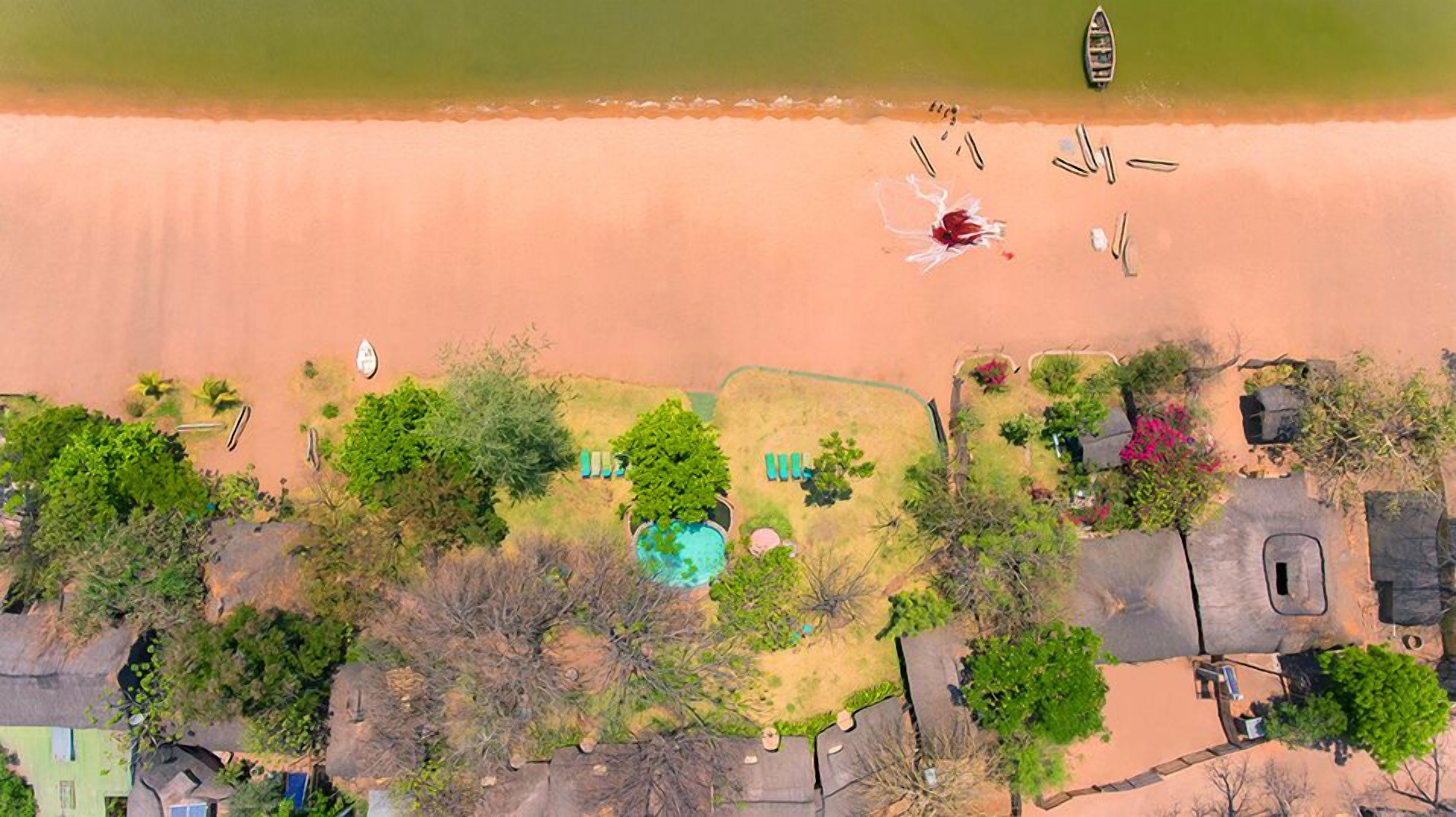 Vue aérienne d’une propriété située sur la côte, avec une piscine, des espaces verts et un bateau sur la plage.