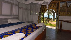 A bedroom with a bed, a mosquito net, and a view of the beach. - Mgoza Lodge (Cape Maclear)