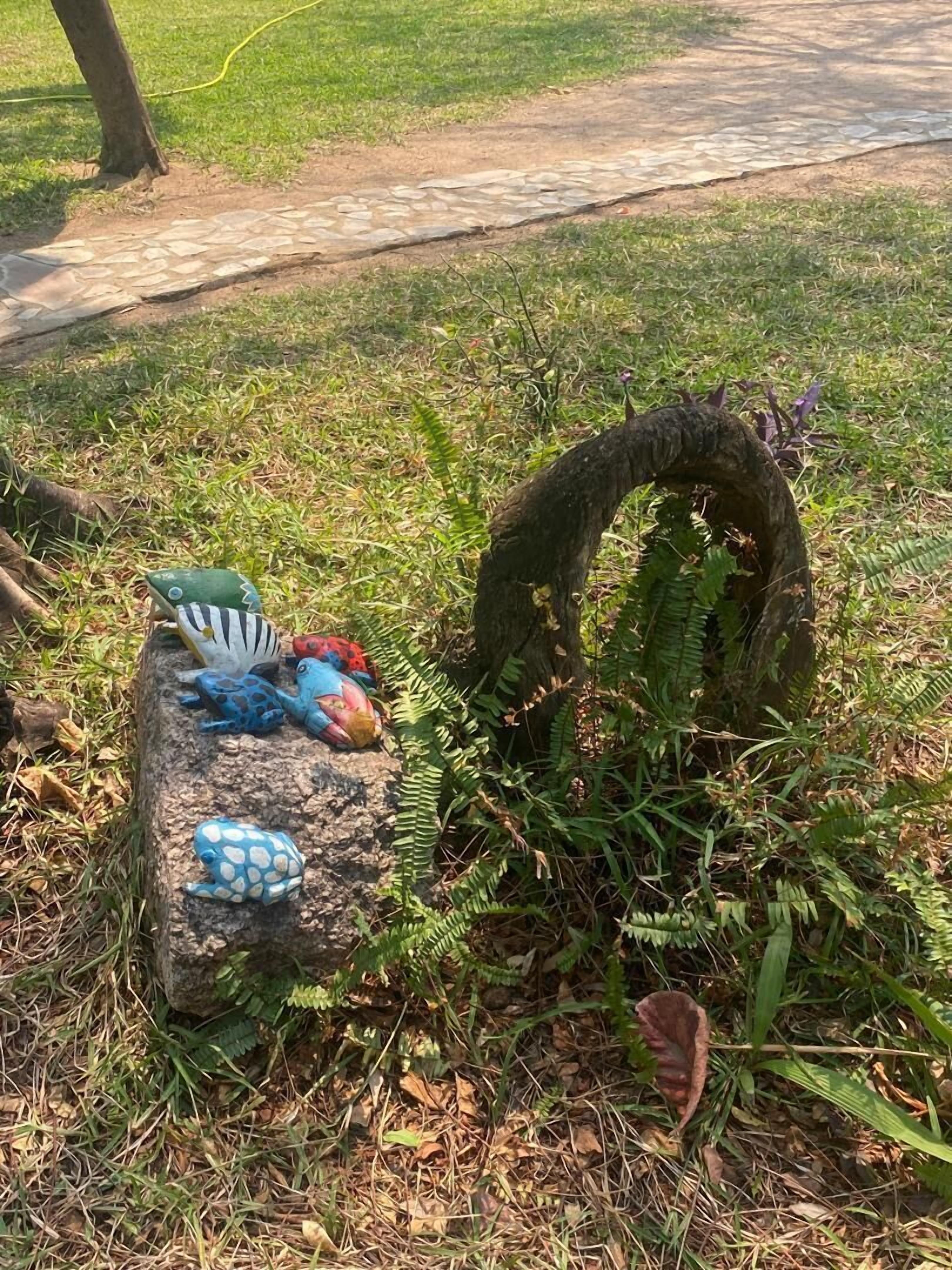 A stone bench with colorful frog sculptures and a curved handle.