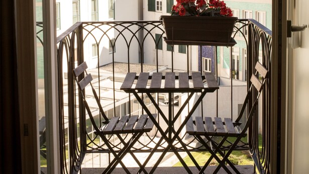 A balcony with a table and chairs, a hanging flower pot, and a view of buildings with a clock tower. - Cardosas Story Apart byPortoCityHosts (Porto)