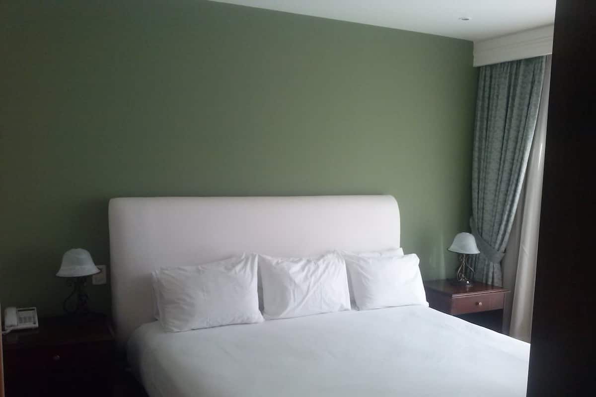 A hotel room with a large bed, two bedside tables, and a window with curtains.