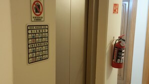 Een lift met nooduitgangsborden, een bord met ‘niet gebruiken bij nood’ en een brandblusser aan de muur.