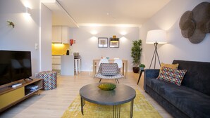 Un salon moderne avec un téléviseur à écran plat, une table basse ronde, un canapé et un coin repas à l’arrière-plan.