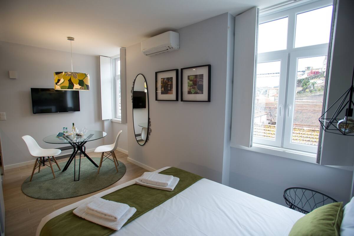 Une chambre d’hôtel moderne, équipée d’un lit, d’un coin repas avec des chaises, d’une télévision et de tableaux encadrés au mur.
